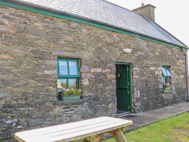 A stone building with green framed windows and a green door with flower boxes under the windows and a wooden picnic table outside at An Nead in Ballinknockane near Dingle County Kerry
