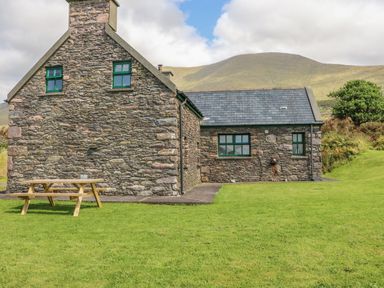 Stone house with green window frames and a wooden picnic table on a lawn at An Nead in Ballinknockane near Dingle County Kerry