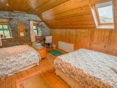 A bedroom with two beds a wooden chest a chair a mirror and windows at An Nead in Ballinknockane near Dingle County Kerry