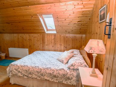 A bedroom with a bed covered in floral bedding under a skylight next to a nightstand with a floral lamp at An Nead in Ballinknockane near Dingle County Kerry