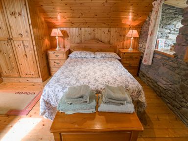 A bedroom with a double bed between two bedside tables with lamps and folded towels on a wooden bench at An Nead Ballinknockane near Dingle County Kerry