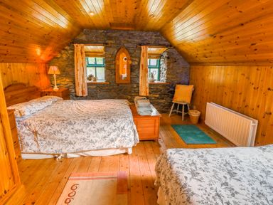 A bedroom with two beds wooden walls and ceiling stone wall with two windows at An Nead Ballinknockane near Dingle County Kerry