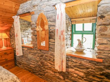 A bedroom corner with stone walls a wooden dresser a lamp a small window with green frame and a decorative pitcher on the sill at An Nead in Ballinknockane near Dingle County Kerry
