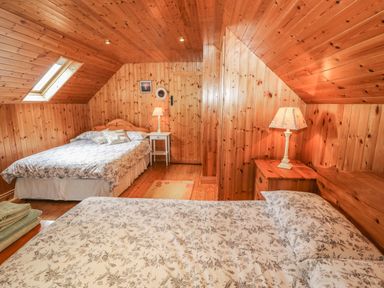 A bedroom with two beds wooden panel walls and ceiling bedside tables and lamps at An Nead Ballinknockane near Dingle County Kerry