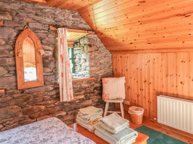 A bedroom corner with a stone wall mirror wooden chair with a cushion folded towels on a bed and a waste basket at An Nead in Ballinknockane near Dingle County Kerry