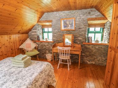 A bedroom with wooden ceiling and floor a bed with folded towels a wooden desk and chair and stone wall at An Nead Ballinknockane near Dingle County Kerry
