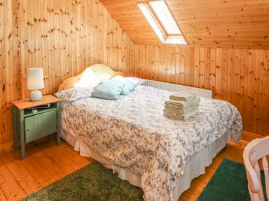 A bedroom with a bed covered with a patterned duvet and two pillows a green bedside table with a lamp folded towels on the bed a skylight window and wooden wall panels at An Nead in Ballinknockane near Dingle County Kerry