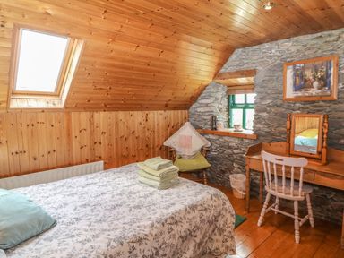 A bedroom with a bed a chair and a wooden dressing table with a mirror at An Nead in Ballinknockane near Dingle County Kerry