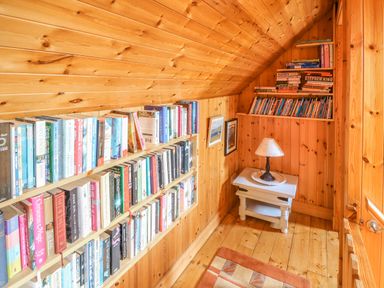 A small wooden room with bookshelves filled with books a small table with a lamp and framed pictures on the wall at An Nead Ballinknockane near Dingle County Kerry