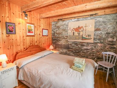 A bedroom with wooden walls and ceiling beams a bed with folded towels on it two bedside tables with lamps and framed pictures on the wall at An Nead in Ballinknockane near Dingle County Kerry