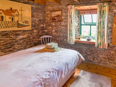 A bedroom with stone walls a bed a chair and a window with curtains at An Nead in Ballinknockane near Dingle County Kerry