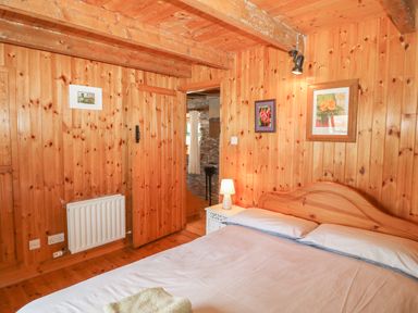 A bedroom with wooden walls and ceiling a bed with pillows a bedside table with a lamp and framed pictures on the walls at An Nead in Ballinknockane near Dingle County Kerry