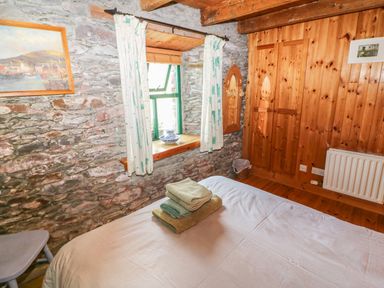 A bedroom with a stone wall window with curtains and folded towels on a bed at An Nead in Ballinknockane near Dingle County Kerry