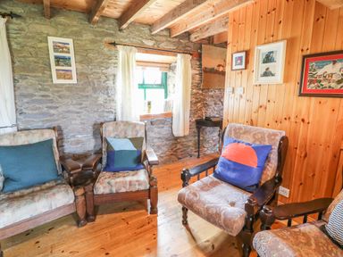 A sitting area with wooden armchairs and cushions in a room with stone and wooden walls at An Nead in Ballinknockane near Dingle County Kerry
