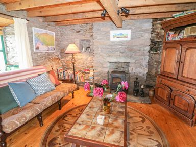 A living room with a tiled coffee table with flowers on it a stone fireplace a wooden cabinet and a sofa with cushions at An Nead in Ballinknockane near Dingle County Kerry