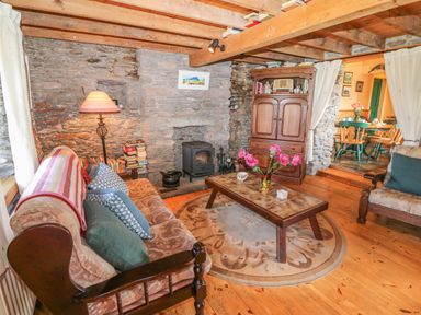 A living room with a stone wall stove wooden coffee table and armchairs at An Nead in Ballinknockane near Dingle County Kerry