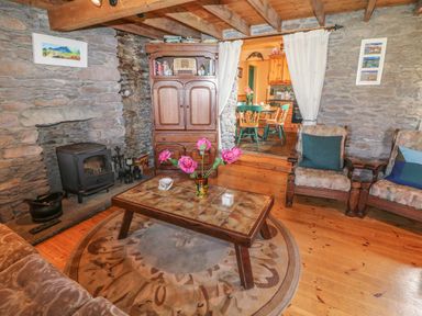 A living room with stone walls a wood stove wooden furniture and a dining area visible through a doorway at An Nead Ballinknockane near Dingle County Kerry