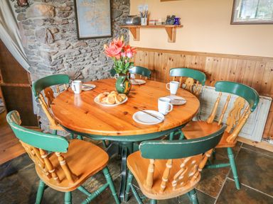 A dining area with a round wooden table set with plates mugs and a vase of flowers surrounded by wooden chairs with green backs at An Nead in Ballinknockane near Dingle County Kerry