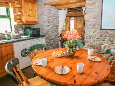A kitchen with a wooden round table set with plates, mugs, a vase of flowers, and a plate of baked goods at An Nead in Ballinknockane near Dingle, County Kerry
