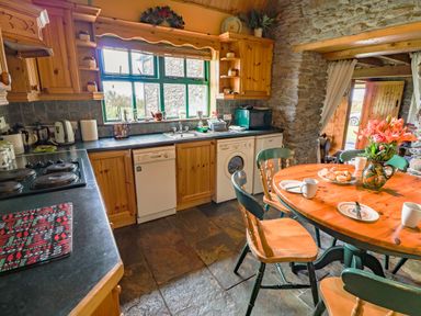A kitchen with wooden cabinets a round wooden table with a flower vase and plates at An Nead in Ballinknockane near Dingle County Kerry