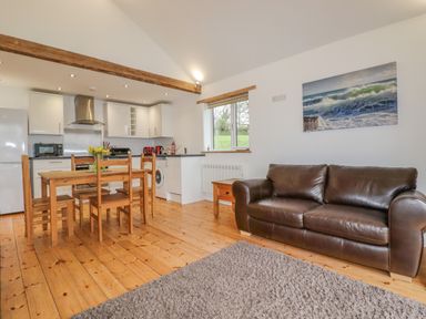 An open plan kitchen and living area with wooden dining table and chairs a brown leather sofa and kitchen appliances at Vine Cottage in St Ewe near Sticker 