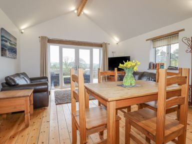 A dining area with wooden table and chairs a vase with flowers a living room with leather sofas a television and french doors at Vine Cottage in St Ewe near Sticker