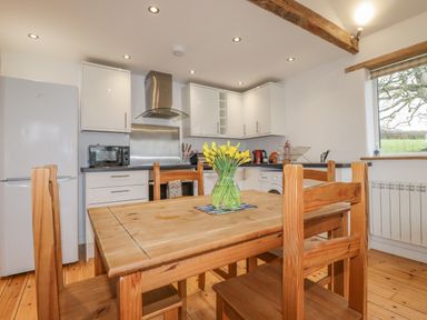 A kitchen with wooden table and chairs and a vase of yellow flowers at Vine Cottage in St Ewe near Sticker 