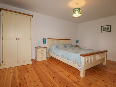 A bedroom with a bed and two bedside tables with lamps and a wardrobe on a wooden floor at Vine Cottage in St Ewe near Sticker 