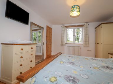 A bedroom with a bed a chest of drawers a mirror a window and a wardrobe at Vine Cottage in St Ewe near Sticker 