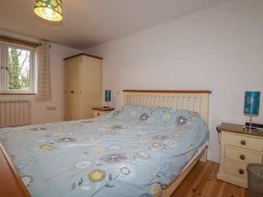 A bedroom with a double bed covered with a floral patterned duvet two bedside tables with lamps a wardrobe and a window at Vine Cottage in St Ewe near Sticker