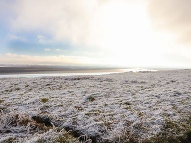 A frosted grassy field with a body of water in the distance under a cloudy sky at Sonya's Cottage Anthorn Solway Firth