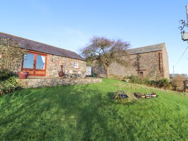 A stone building with a patio table and chairs on a raised stone terrace and grass lawn at Sonya's Cottage in Anthorn Solway Firth