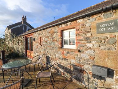 A stone exterior wall with window and door and outdoor table and chairs at Sonya's Cottage in Anthorn Solway Firth