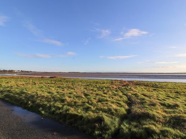 A grassy field next to a body of water under a clear sky at Sonya's Cottage in Anthorn Solway Firth