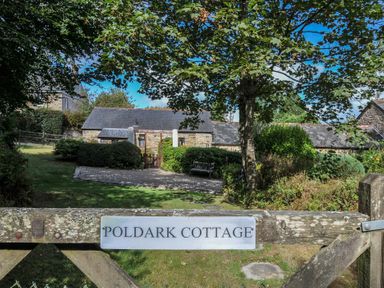 A cottage with a pathway and bench surrounded by trees at Poldark Cottage East Taphouse