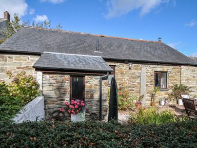 An outdoor view of a stone cottage with flowers by the window at Poldark Cottage East Taphouse
