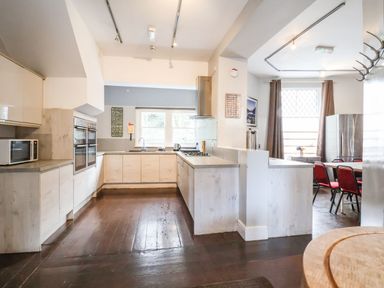 A kitchen with wooden cabinets a microwave built in ovens a gas stove and a dining area with red chairs at Mountain View Penmaenmawr