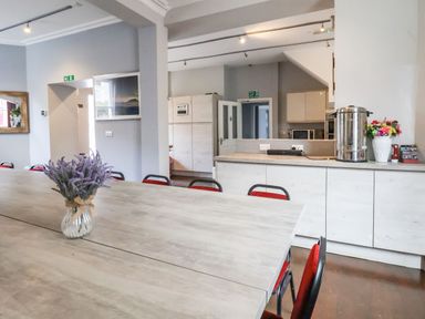A dining area with tables and chairs a kitchen area with cabinets and appliances and flower vases at Mountain View in Penmaenmawr