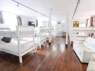 A dormitory room with multiple white bunk beds and a white sofa on wooden floor at Mountain View in Penmaenmawr