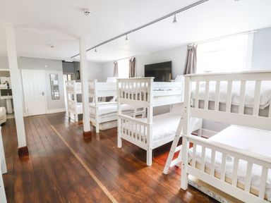 A bedroom with multiple white bunk beds wooden floors and windows with curtains at Mountain View in Penmaenmawr