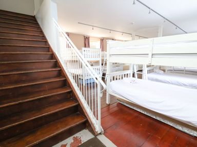 A room with wooden stairs and multiple white bunk beds with white bedding at Mountain View in Penmaenmawr