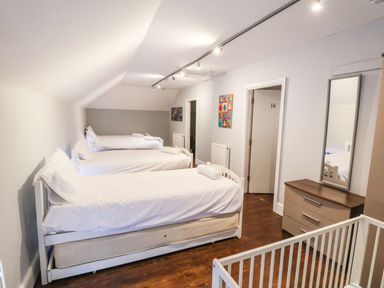 A bedroom with three single beds with white bedding a dresser with a mirror and a crib at Mountain View in Penmaenmawr