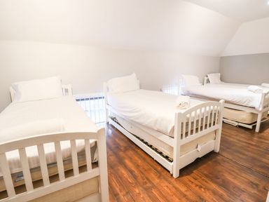 A bedroom with three white single beds on wooden floor at Mountain View in Penmaenmawr