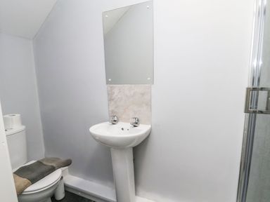 A small bathroom with a pedestal sink, mirror, toilet with a towel and two toilet paper rolls and a shower door at Mountain View in Penmaenmawr