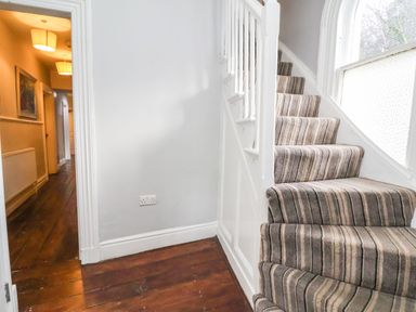 A staircase with striped carpet next to a hallway with wooden floor at Mountain View in Penmaenmawr