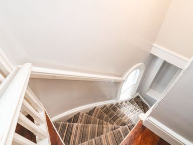A carpeted staircase with striped pattern and white banisters near a window at Mountain View in Penmaenmawr