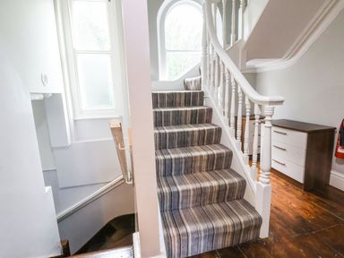 A staircase with striped carpet and white banister next to a wooden floor and white drawers at Mountain View in Penmaenmawr