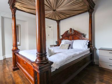 A bedroom with a wooden four-poster bed with white bedding and a small dresser at Mountain View in Penmaenmawr