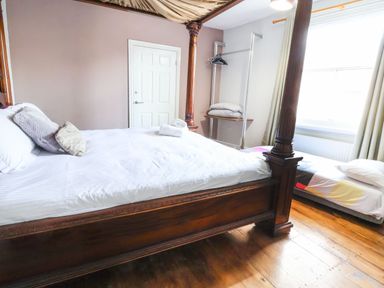 A bedroom with a four poster bed white linens a single bed near a window and an open clothes rack at Mountain View in Penmaenmawr