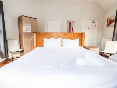 A bedroom with a large bed pillows rolled towels two chairs wardrobe dresser and two doors at Mountain View in Penmaenmawr